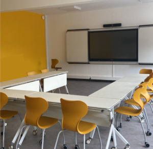 Salle équipée de tables modulables, chaises mobiles et de tableaux blancs coulissants avec un écran interactif au centre